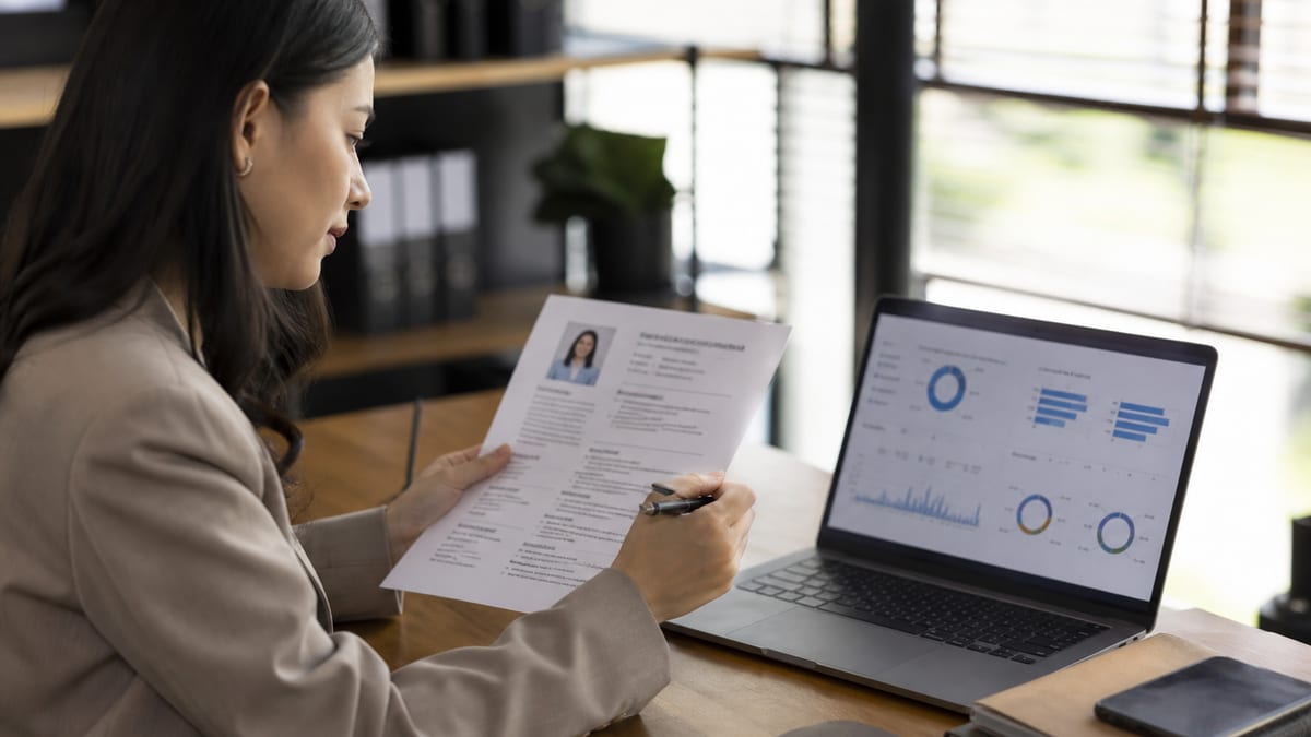 Recruiter reviewing a printed resume next to a laptop scoring dashboard
