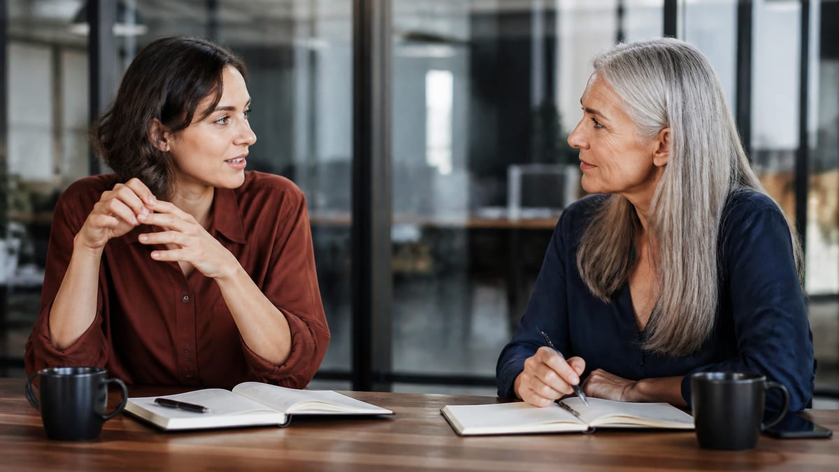 Two colleagues talking across a conference table with notebooks