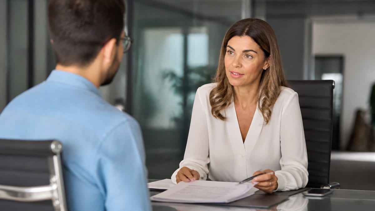 Employee and manager meeting across a glass office desk with a folder