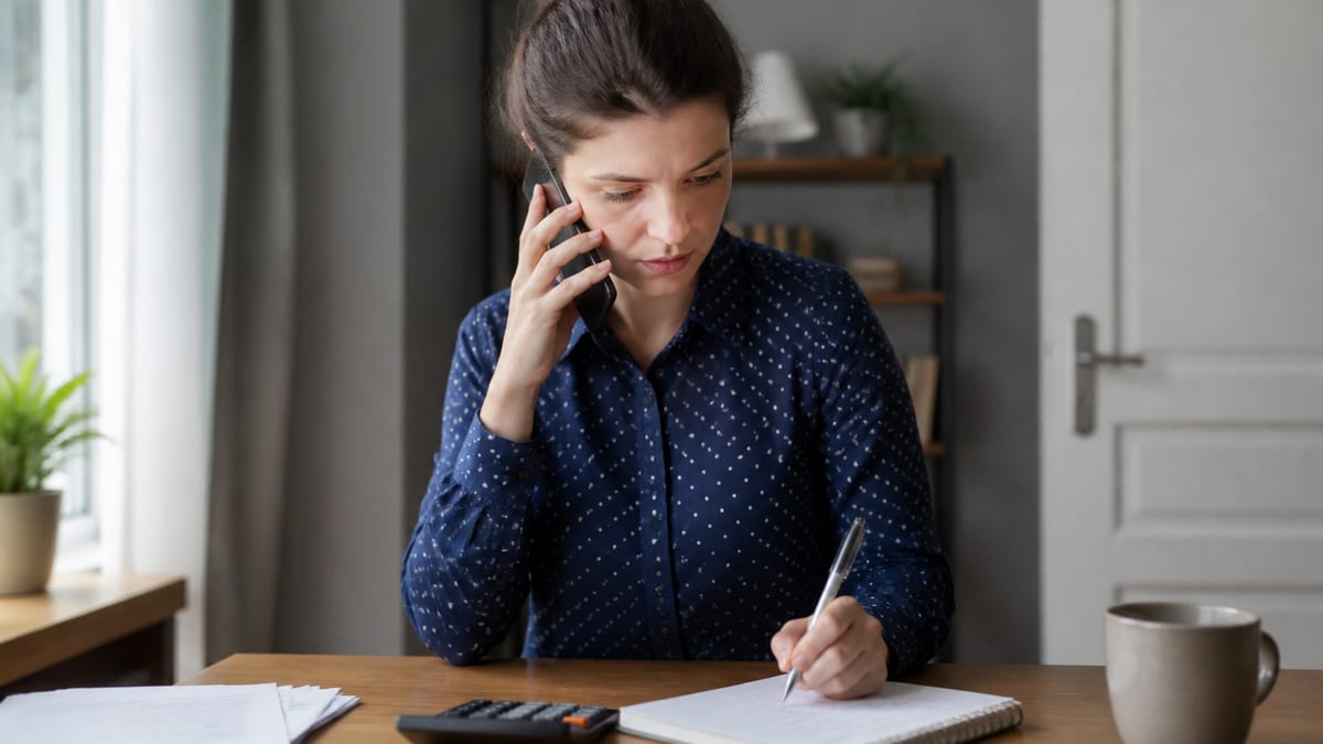 Person on a phone call with a notepad and calculator at a home office