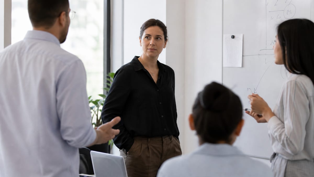 Team lead listening in a small standup meeting around a whiteboard
