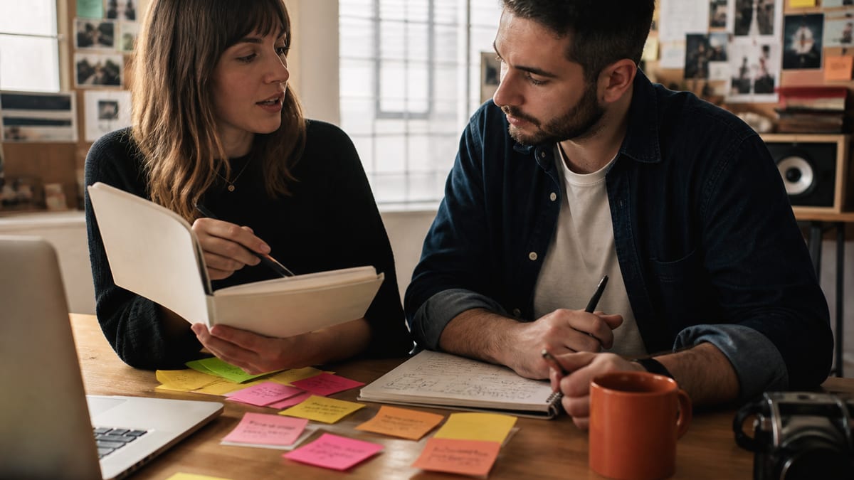 Creative professional brainstorming with sticky notes, sketchbook, and laptop